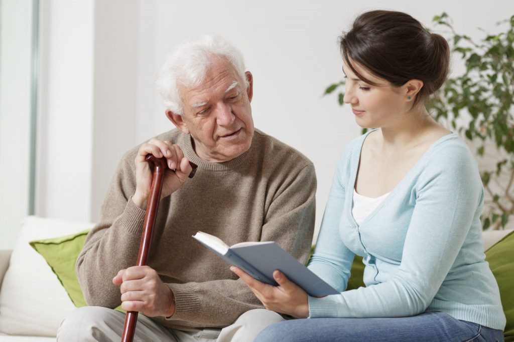 Cuidadora de adultos mayores leyéndole un libro a un adulto mayor
